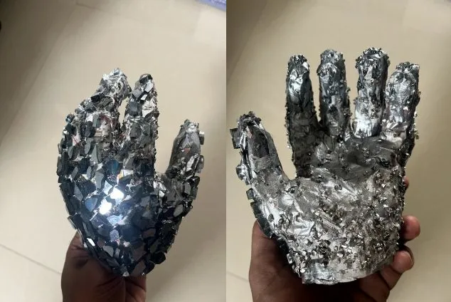 Two views of a hand sculpture covered in mirrored chips and metallic shards.