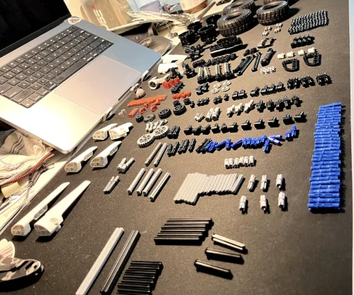 A laptop beside a large spread of small mechanical and electronic parts laid out on a black table.